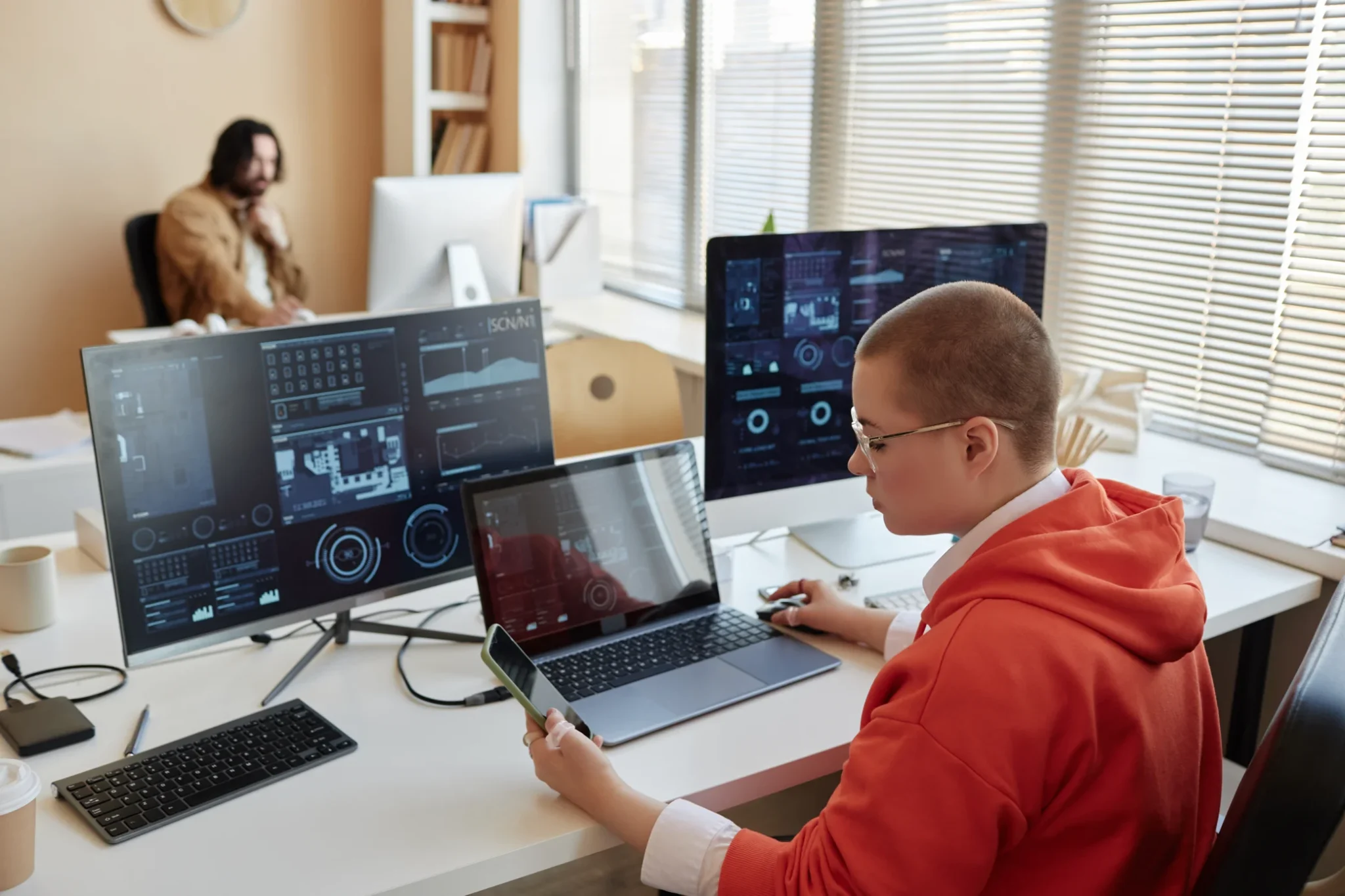 Person working at a desk with multiple computer screens in an office environment.